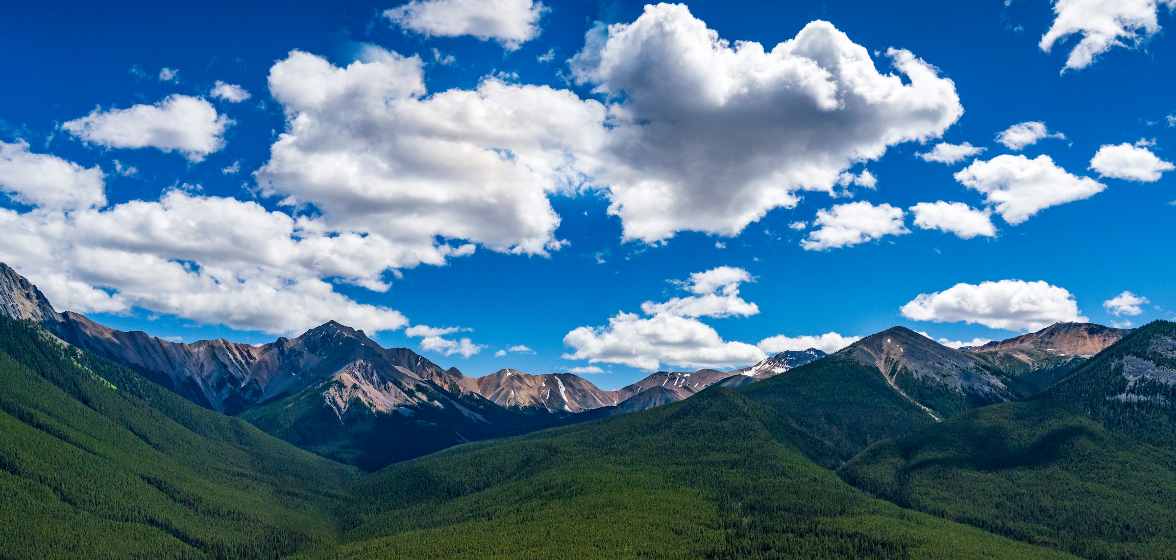 Sweeping mountain landscape with blue sky, white clouds, and forested slopes used to demonstrate colour filter effects in black and white photography